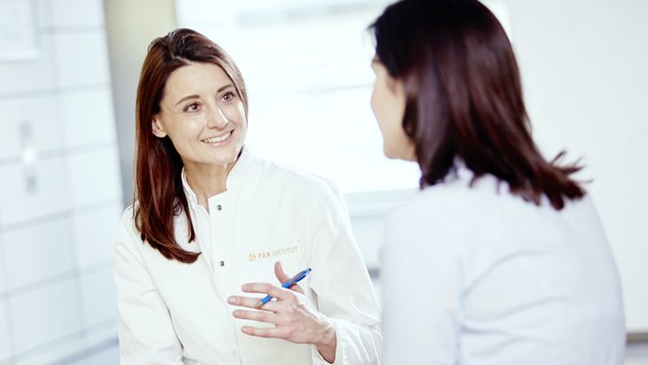 A healthcare professional wearing a white coat is engaged in a conversation with a patient. The setting appears to be a medical office, emphasizing a supportive and informative dialogue. The focused expressions suggest a discussion about health or treatment options.