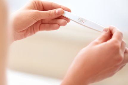 A person holds a pregnancy test displaying one bold line and a faint second line, indicating a potential positive result. The background is softly blurred, emphasizing the test and the person's hands.