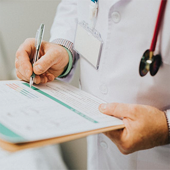 Eine Person in einem weißen Kittel hält ein Clipboard mit einem Formular und schreibt mit einem Stift darauf. Das Bild vermittelt den Eindruck einer medizinischen Untersuchung oder Dokumentation.