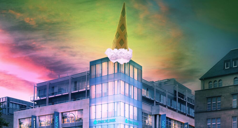 A modern building with a triangular spire topped by a large ice cream cone stands amidst adjacent structures. The sky above features vibrant colors, adding an artistic touch to the urban scene.