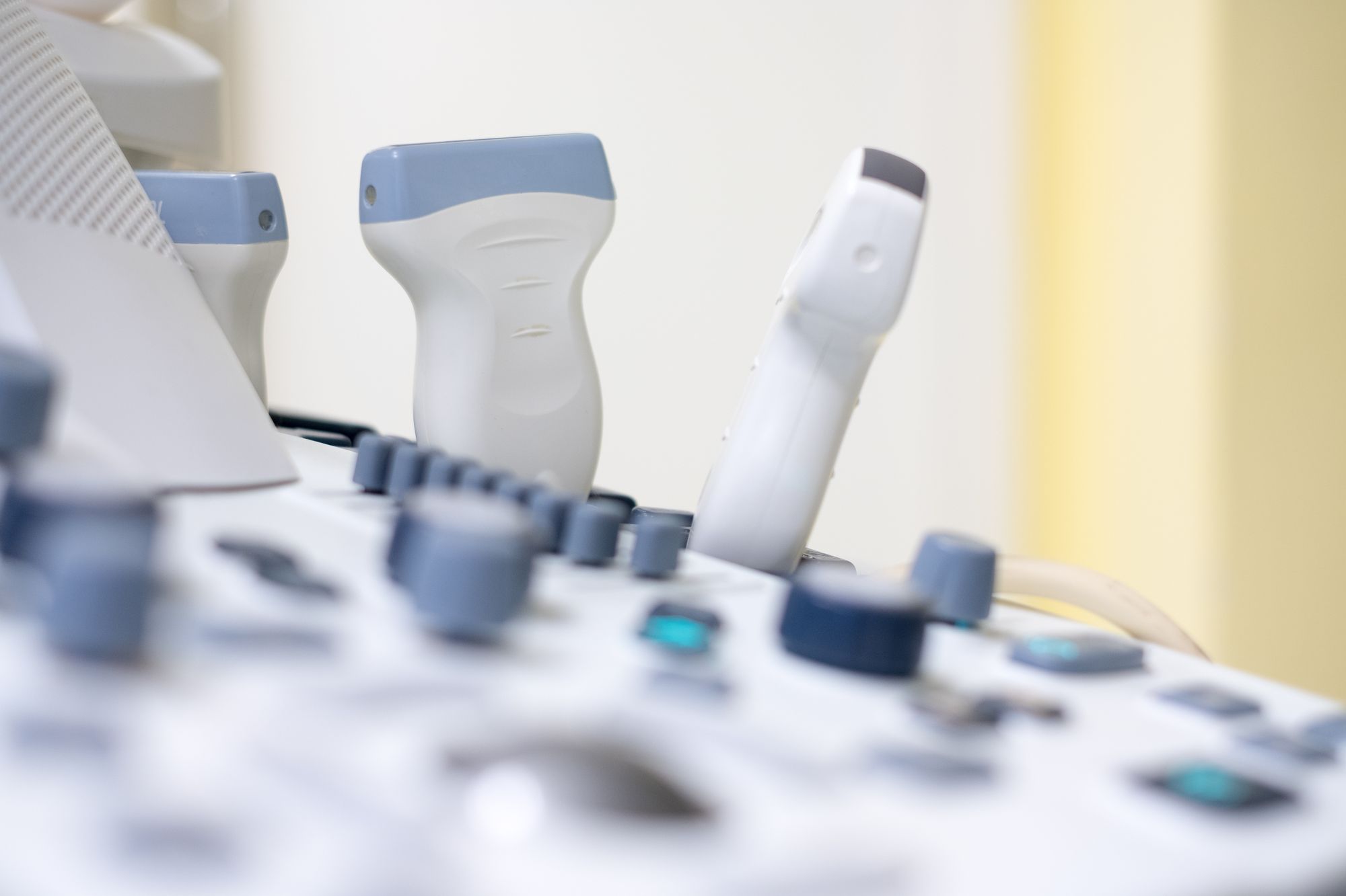 The image shows a close-up view of a medical ultrasound machine. It features control knobs and transducers, which are handheld devices used to capture images during ultrasound examinations. The backdrop is softly blurred, emphasizing the equipment's details.