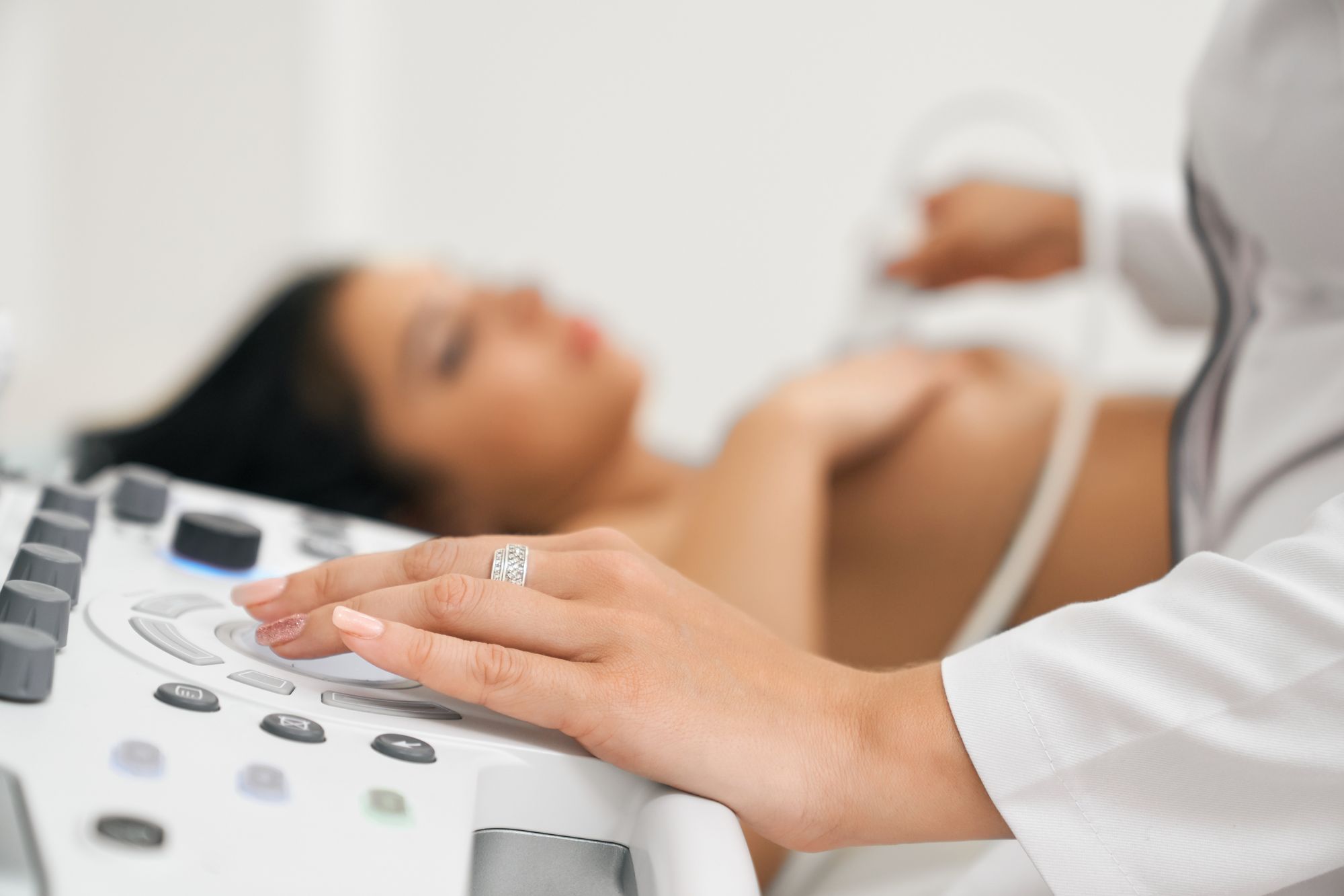 A medical professional is performing an ultrasound procedure on a patient lying down. The focus is on the technician's hand adjusting the ultrasound machine while the patient appears relaxed.