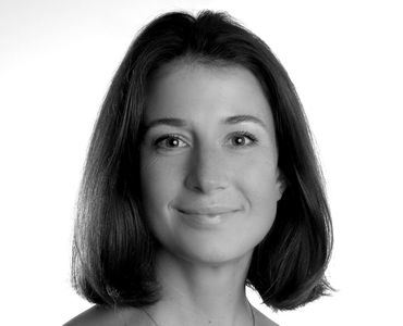 Eine schwarz-weiße Porträtaufnahme einer Frau mit mittellangen, glatten Haaren. Sie hat einen sanften Ausdruck und trägt ein schwarzes Shirt. Der Hintergrund ist einfarbig und hell, was den Fokus auf ihr Gesicht lenkt.