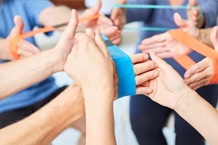 A group of hands holds colorful resistance bands, working together in a coordinated exercise. The scene emphasizes collaboration and engagement in physical activity.