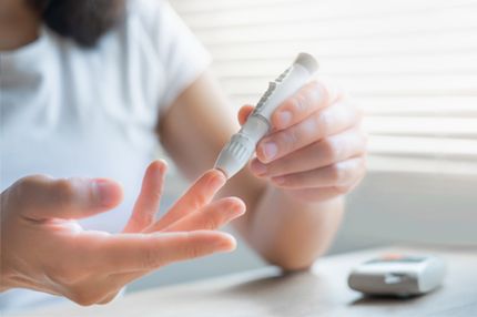 A person prepares to check their blood glucose levels by using a lancing device on their fingertip. The setting suggests a home environment with soft lighting, highlighting the act of self-monitoring health.