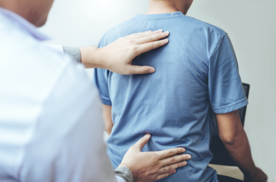 A healthcare professional is gently placing hands on the back of a seated patient, suggesting a therapeutic or assessment session. The patient is wearing a blue shirt, focused on receiving care or treatment.