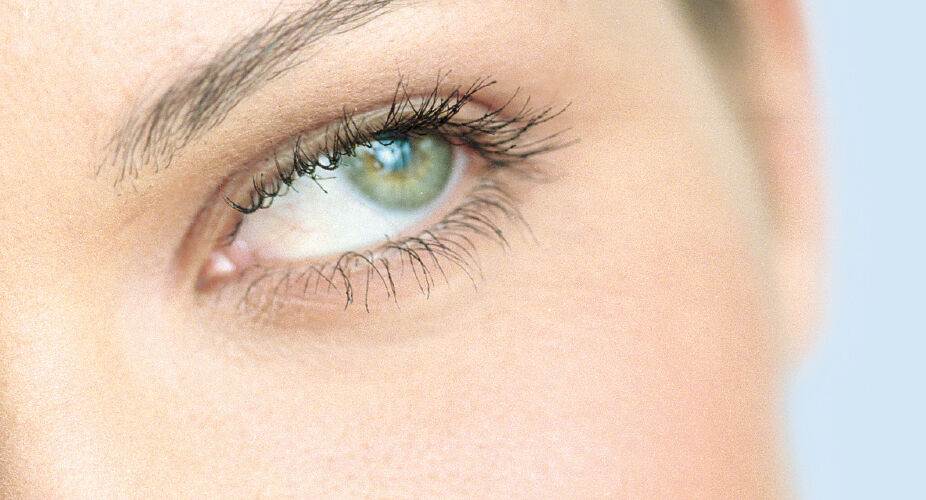 A close-up of a person's eyes, highlighting their vibrant green color and long eyelashes. The background features a soft blue tone, emphasizing the focus on the eyes. The expression conveys curiosity or contemplation.